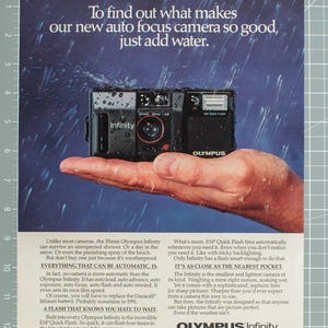 May include: A black Olympus Infinity 35mm auto focus camera with a Zuiko 35mm lens, featuring the text 'Infinity' and 'ESP QUICK FLASH'. The camera is wet, positioned against a rainy background with promotional text below it.