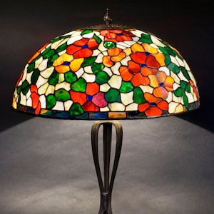 May include: A stained glass table lamp with a floral design in shades of red, orange, green, and white. The lamp has a bronze base with a decorative design.