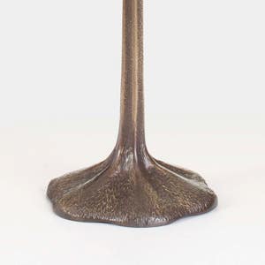 May include: A brown metal lamp base with a tall, slender stem and a wide, flat base that resembles a foot.