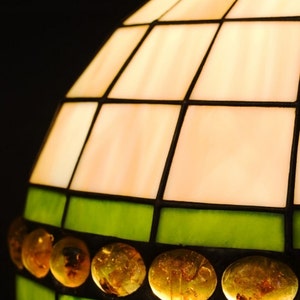 May include: A stained glass lampshade with a white and green geometric pattern. The shade is decorated with amber glass beads and the text "e-witraze.pl" is printed on the bottom.
