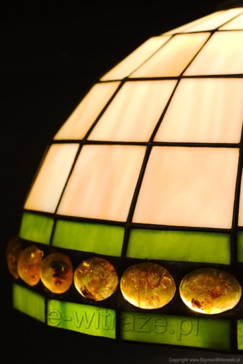 May include: A stained glass lampshade with a white and green geometric pattern. The shade is decorated with amber glass beads and the text "e-witraze.pl" is printed on the bottom.
