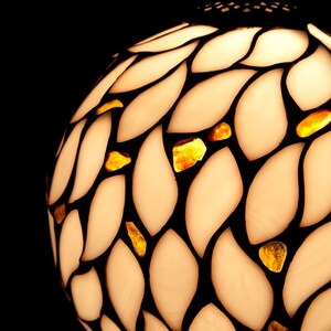 K&ouml;nnte beinhalten: Ein wei&szlig;er Glaslampenschirm mit einem schwarzen Blattmotiv und bernsteinfarbenen Glasakzenten. Der Lampenschirm ist rund und hat eine strukturierte Oberfl&auml;che.