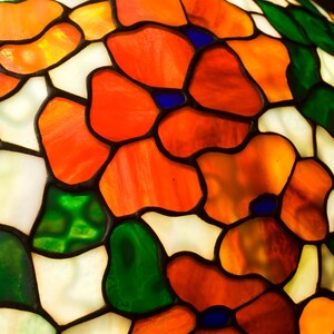 May include: A stained glass lampshade with a floral design. The shade features red, orange, green, and white glass pieces. The glass is cut into various shapes and sizes, creating a unique and intricate pattern.