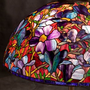 May include: A stained glass lampshade with a floral design featuring purple, blue, red, and green colors. The lampshade is made of glass and has a metal frame.