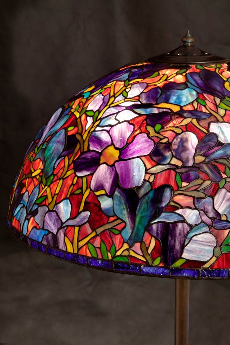 May include: A stained glass lampshade with a floral design featuring purple, blue, red, and green colors. The lampshade is made of glass and has a metal frame.