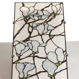 May include: A stained glass panel depicting white magnolia blossoms with green leaves and brown branches on a white background.