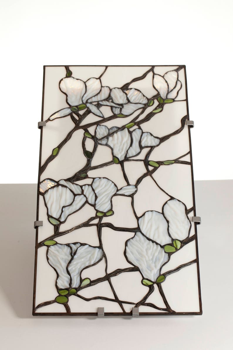 May include: A stained glass panel depicting white magnolia blossoms with green leaves and brown branches on a white background.