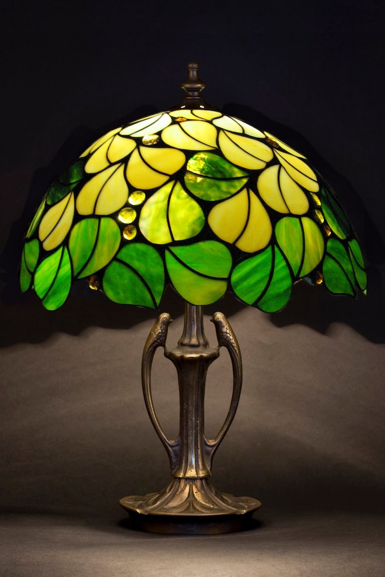 May include: A stained glass table lamp with a green and yellow floral design. The lamp has a bronze base with a decorative design.
