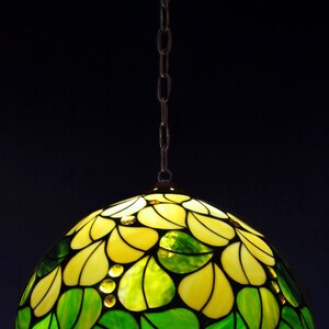 May include: A stained glass pendant light with a yellow and green floral design. The light is hanging from a chain.