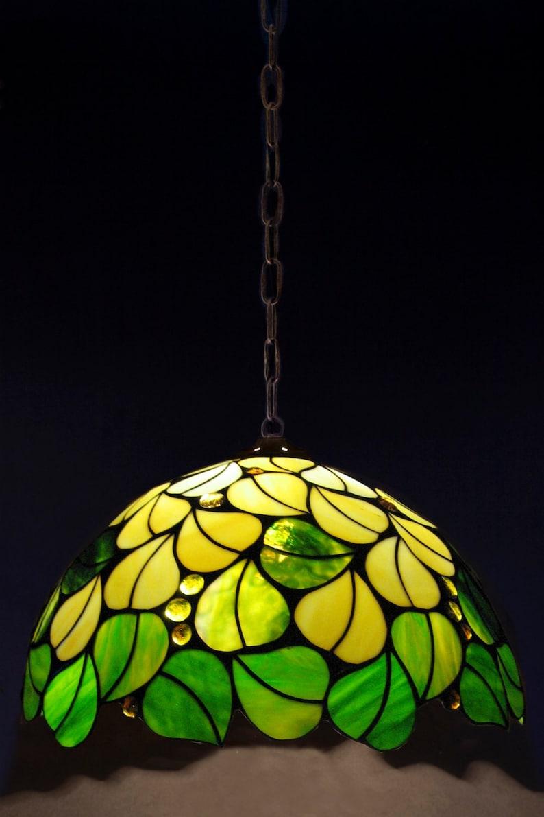 May include: A stained glass pendant light with a yellow and green floral design. The light is hanging from a chain.