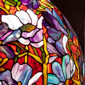 May include: A stained glass lampshade with a floral design. The shade features a variety of colors, including red, blue, purple, yellow, and green. The flowers are stylized and have a whimsical feel.