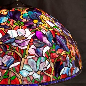 May include: A stained glass lampshade with a floral design featuring purple, blue, red, and green flowers. The lampshade is made of glass and has a metal frame.