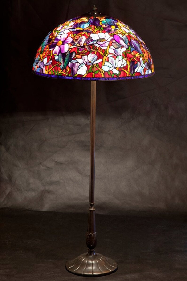 May include: A stained glass floor lamp with a floral design featuring white, purple, and red flowers. The lamp has a dark brown metal base and a tall, slender stem.