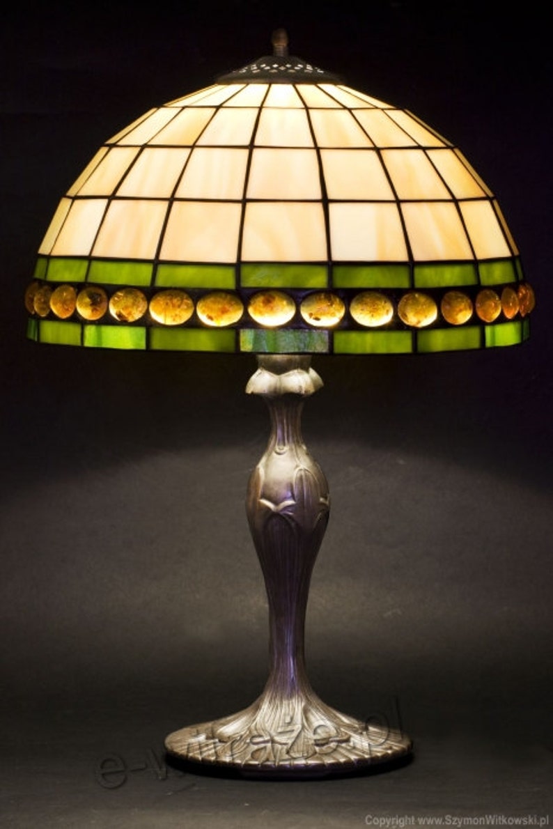 May include: A Tiffany-style table lamp with a stained glass shade featuring a geometric pattern in shades of green and amber. The base is made of metal and has a floral design.