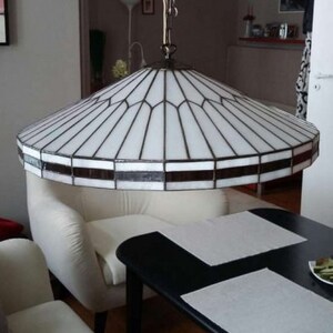 Puede incluir: Una l&aacute;mpara de techo de cristal blanco con un marco de metal negro cuelga sobre un sof&aacute; blanco y una mesa negra con manteles individuales blancos.