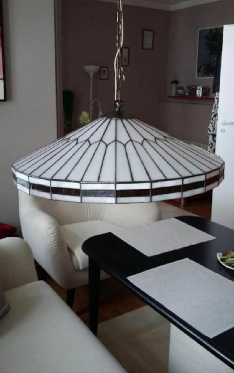 Puede incluir: Una l&aacute;mpara de techo de cristal blanco con un marco de metal negro cuelga sobre un sof&aacute; blanco y una mesa negra con manteles individuales blancos.