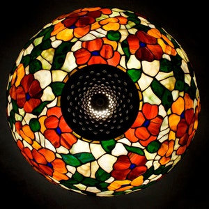 May include: A stained glass lampshade with a floral design featuring red, orange, yellow, green, and blue flowers. The lampshade is round and has a metal frame.