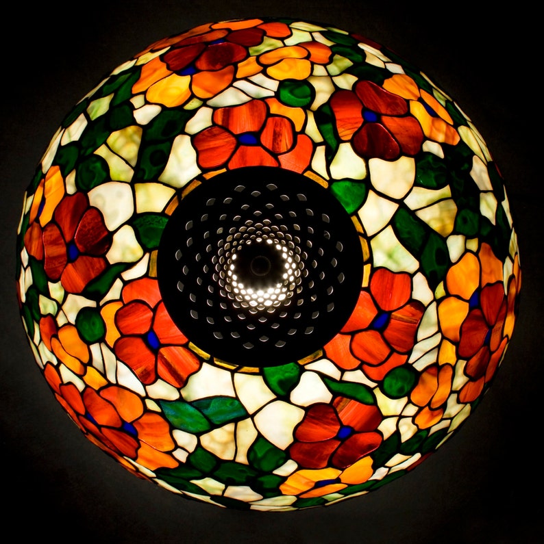 May include: A stained glass lampshade with a floral design featuring red, orange, yellow, green, and blue flowers. The lampshade is round and has a metal frame.
