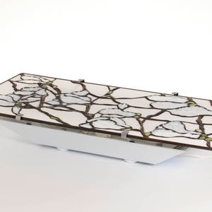 May include: A white ceiling light fixture with a stained glass shade featuring a floral design of white blossoms and brown branches. The shade is attached to a white base with silver clips.