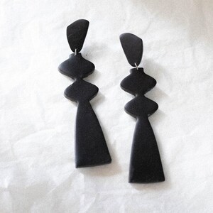 Könnte beinhalten: Ein Paar schwarze geometrische Ohrhänger. Die Ohrringe sind aus Polymer Clay gefertigt und haben ein modernes, abstraktes Design.