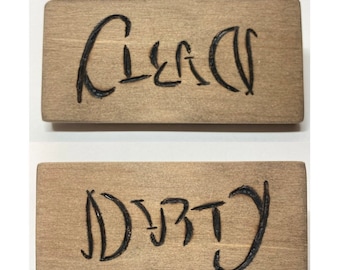 May include: Two wooden signs with the words "Clean" and "Dirty" burned into the surface. The signs are light brown with a wood grain texture.