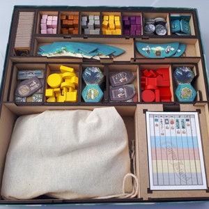 May include: A wooden game organiser with compartments for storing game pieces. The organiser has a light blue exterior and a brown interior. The compartments are filled with various coloured game pieces, including red, blue, green, yellow, and brown. There is a white cloth bag in the centre compartment.
