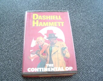Puede incluir: Un libro antiguo de tapa dura titulado "The Continental Op" de Dashiell Hammett. La portada roja presenta texto amarillo y una ilustración retro de dos figuras. Los bordes del libro muestran desgaste.