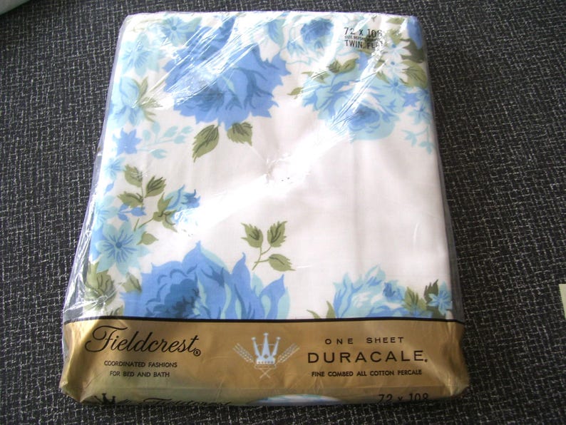 Puede incluir: Una s&aacute;bana blanca empaquetada en pl&aacute;stico transparente con un estampado floral azul y hojas verdes. La etiqueta dorada dice Fieldcrest, Duracale, Fine Combed All Cotton Percale y 72 x 108 Twin Flat. La s&aacute;bana est&aacute; doblada cuidadosamente dentro del pl&aacute;stico.