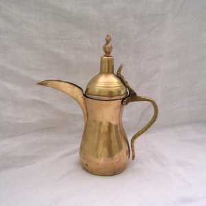 May include: A traditional brass coffee pot with a hinged lid and a decorative finial. The pot has a rounded body and a curved spout.