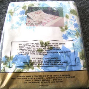 Puede incluir: Un juego de s&aacute;banas Fieldcrest empaquetadas. El embalaje es de pl&aacute;stico transparente, revelando un vistazo al patr&oacute;n floral en el interior. Las s&aacute;banas presentan un fondo blanco con dise&ntilde;os florales azules y verdes. El texto en el embalaje proporciona detalles.