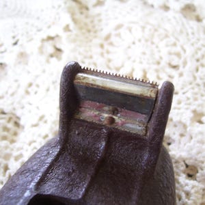 May include: Close-up of a vintage brown tape dispenser. The dispenser has a serrated blade for cutting tape and a textured surface. The image is set against a white, lace-like background.