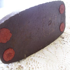 May include: Close-up of the bottom of a dark brown, rectangular object with three red, circular pads. The object has a textured surface and appears to be made of a dense material.