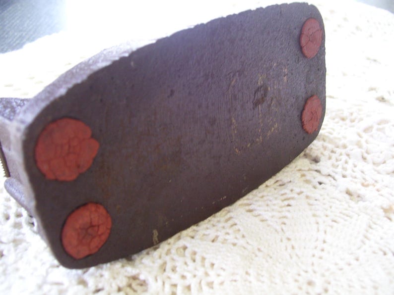 May include: Close-up of the bottom of a dark brown, rectangular object with three red, circular pads. The object has a textured surface and appears to be made of a dense material.