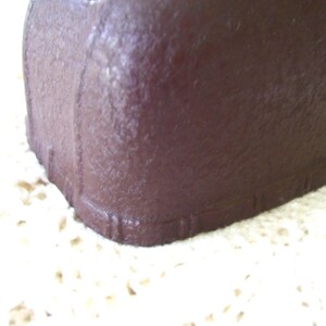 May include: Close-up of a dark brown, rectangular object with a textured surface. The object has rounded corners and vertical lines along the edges. The object is resting on a cream-colored, textured surface.