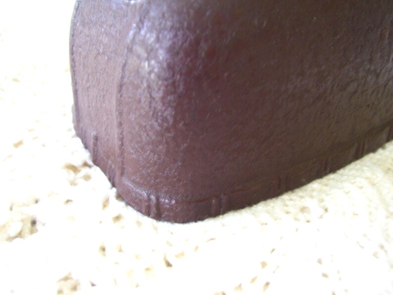 May include: Close-up of a dark brown, rectangular object with a textured surface. The object has rounded corners and vertical lines along the edges. The object is resting on a cream-colored, textured surface.