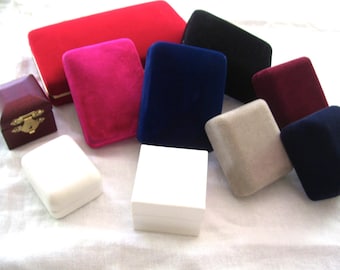 May include: A collection of various jewelry boxes in multiple colors and textures, including red, hot pink, navy blue, black, burgundy, beige, and white. The boxes feature velvet, matte, and smooth finishes, with one small box displaying a gold metal latch.