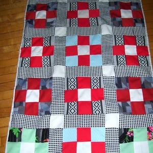 May include: A patchwork quilt with a checkered pattern in black, white, red, and blue. The quilt is made of squares of different fabrics sewn together.