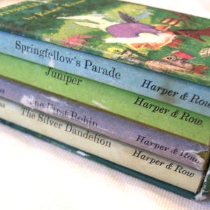 May include: A boxed set of four children's books by Robert Kraus, featuring titles Springfellow's Parade, Juniper, The First Robin, and The Silver Dandelion. The spines are light blue, green, lavender, and white, all published by Harper & Row.