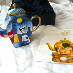 May include: A blue and white porcelain teapot with a cat and a dog design. The teapot is in a box with a label that says "Tea Time Treasures".