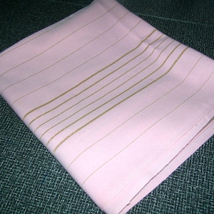 May include: A pink fabric tablecloth with thin gold stripes. The tablecloth is folded and lying on a dark green surface.