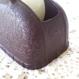 May include: Close-up of a dark brown, textured object with a rounded shape and a recessed area. The object appears to be made of a solid material and has a matte finish. A white, spherical object is partially visible inside the recessed area.