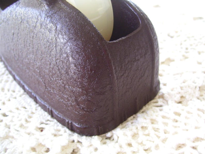 May include: Close-up of a dark brown, textured object with a rounded shape and a recessed area. The object appears to be made of a solid material and has a matte finish. A white, spherical object is partially visible inside the recessed area.