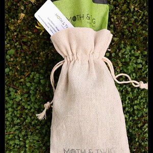 K&ouml;nnte beinhalten: Eine kleine, cremefarbene, Kordelzugtasche mit dem Aufdruck "MOTH & TWIG Handmade in Ireland" auf der Vorderseite. Die Tasche liegt auf einem Bett aus gr&uuml;nem Moos.