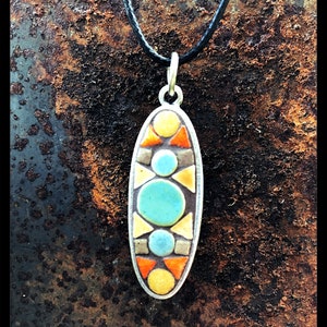 K&ouml;nnte beinhalten: Eine Halskette mit einem Anh&auml;nger in Form eines Ovals aus Mosaikfliesen. Der Anh&auml;nger zeigt ein geometrisches Design mit gelben, orangefarbenen, blauen und grauen Fliesen.