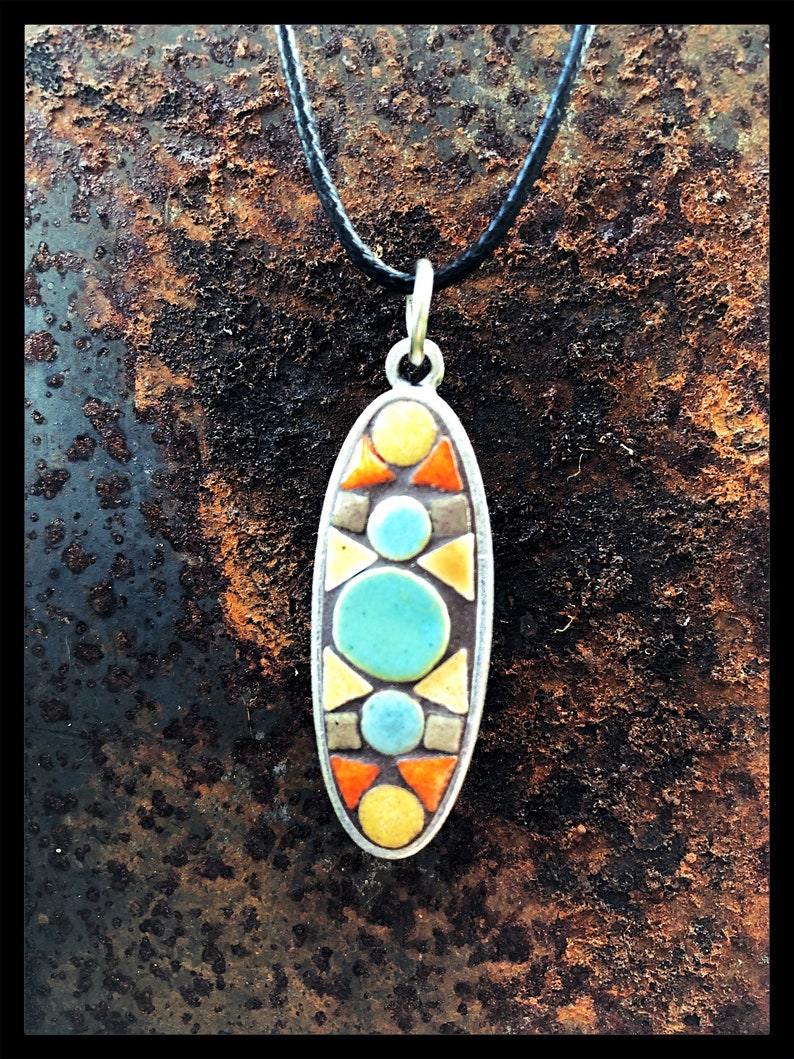 K&ouml;nnte beinhalten: Eine Halskette mit einem Anh&auml;nger in Form eines Ovals aus Mosaikfliesen. Der Anh&auml;nger zeigt ein geometrisches Design mit gelben, orangefarbenen, blauen und grauen Fliesen.