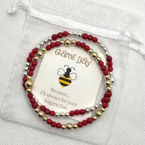 May include: A red and gold beaded bracelet with a small card that says "Game Day" and "Because... I'll always be your biggest fan."
