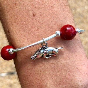 May include: A silver bangle bracelet with two red beads and a silver charm of a running boar.
