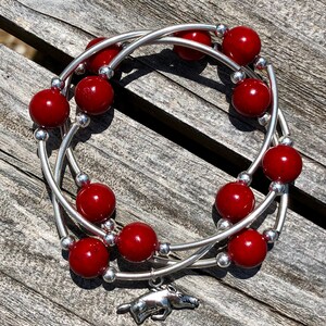 May include: A triple-wrap bracelet with red beads and silver accents. A silver charm of a running boar is attached to the bracelet.
