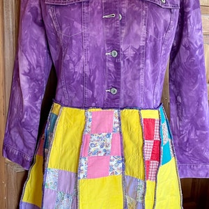 May include: A purple denim jacket with a patchwork quilt skirt. The jacket has a tie-dye pattern and the skirt is made of various fabrics in shades of yellow, pink, and purple.