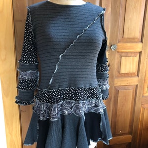 May include: A gray and black striped tunic with a ruffled hem. The tunic has a black and white polka dot pattern on the sleeves and a black paisley pattern on the bottom.